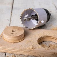 Drilling metal hole saw in a piece of wood. Making holes in a carpentry workshop. Dark background.